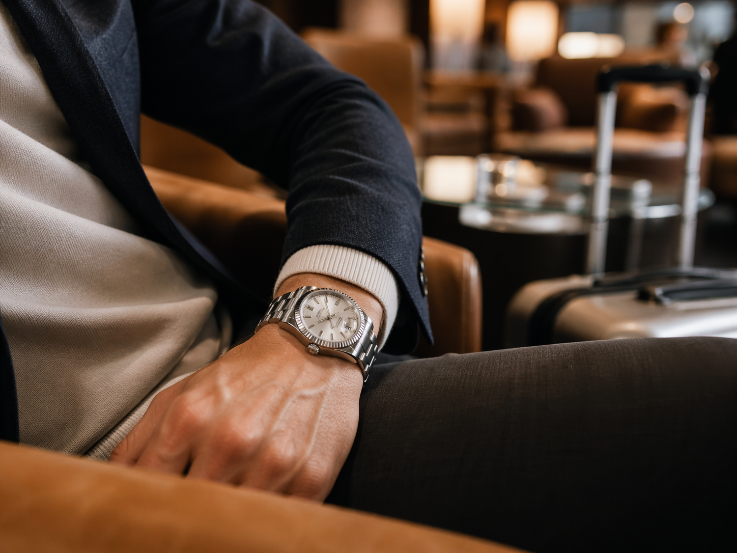Rolex-style replica watch in a travel lounge setting showing refined business casual wear
